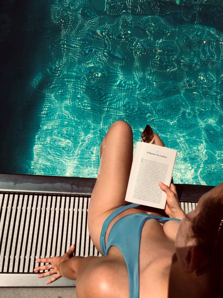 Дівчина біля басейну читає книжку, на ній блакитний купальник жіночий
